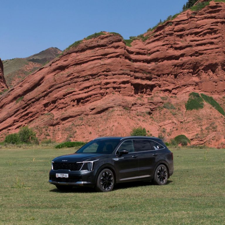 A sleek black Kia Sorento SUV parked against the stunning backdrop of Kyrgyzstan's Jeti Oguz red rock formations.