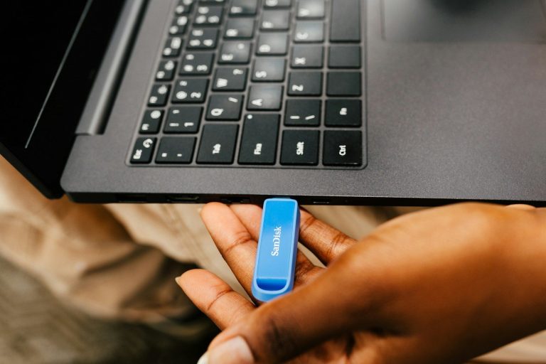 A hand inserting a blue usb drive into a laptop.